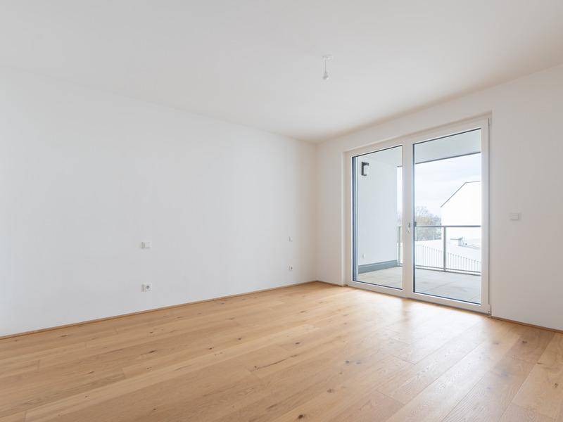 Helles Schlafzimmer mit Holzparkettboden und direktem Zugang zu einem Balkon.