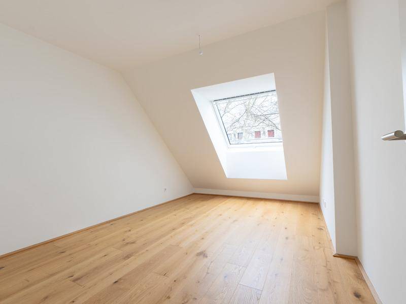 Helles Schlafzimmer im Dachgeschoss mit schräger Decke und einem Dachfenster.