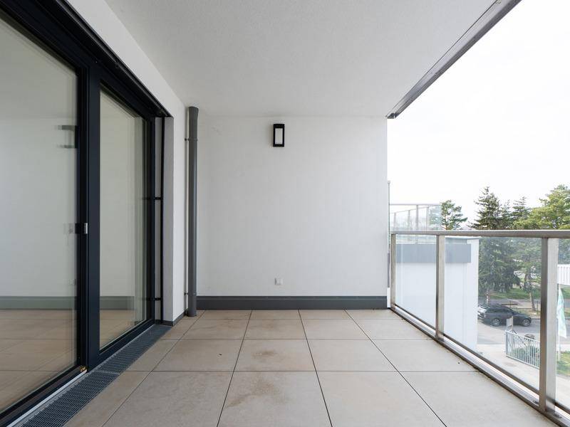 Geräumiger Balkon mit Fliesenboden und Glasgeländer, bietet einen Blick ins Grüne.