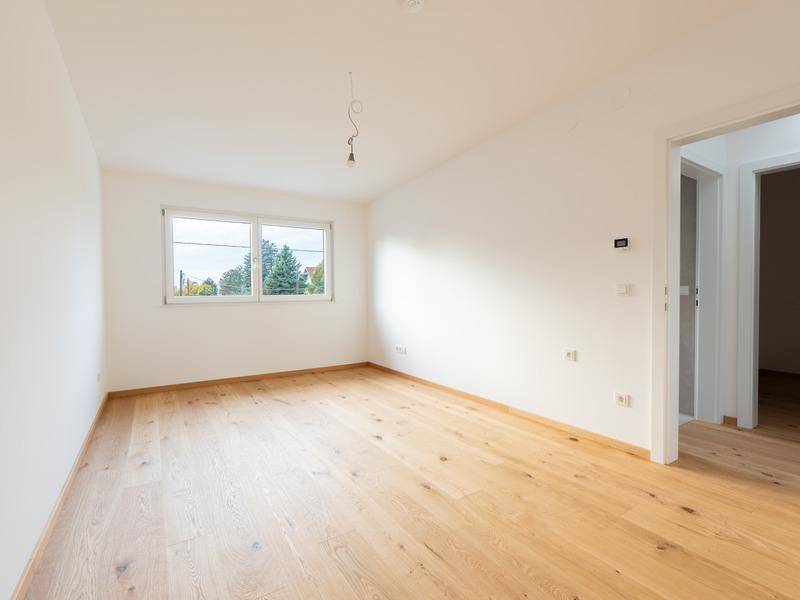 Leeres Schlafzimmer mit hellem Eichenparkettboden und Fenster mit Blick ins Grüne.