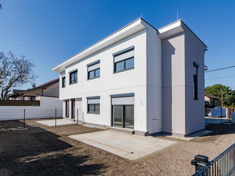 Moderne Doppelhaushälfte von der Seite mit Garten, Rasenfläche und Beton-Terrasse.