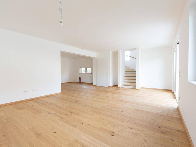Helles, leeres Wohnzimmer mit Eichenparkettboden, großen Fenstern und Treppenaufgang.