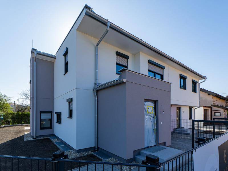 Seitenansicht einer modernen Doppelhaushälfte mit Eingangsbereich und Regenrinne.