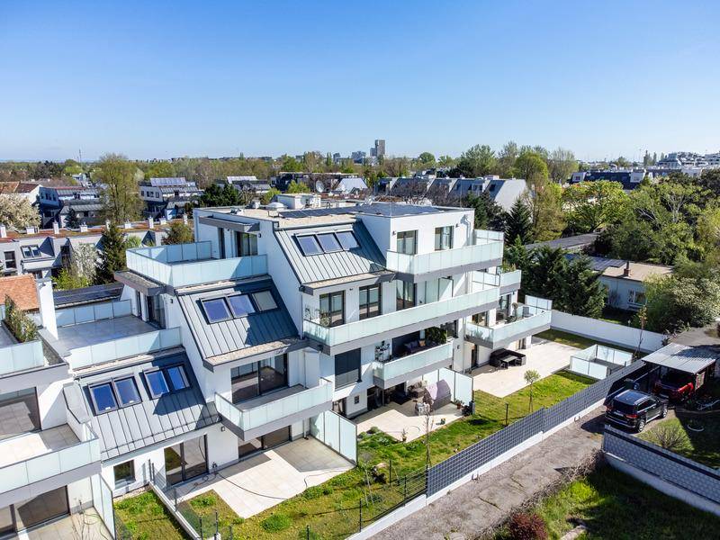 Luftaufnahme einer modernen Wohnanlage mit Balkonen, Terrassen und umliegender Grünfläche.