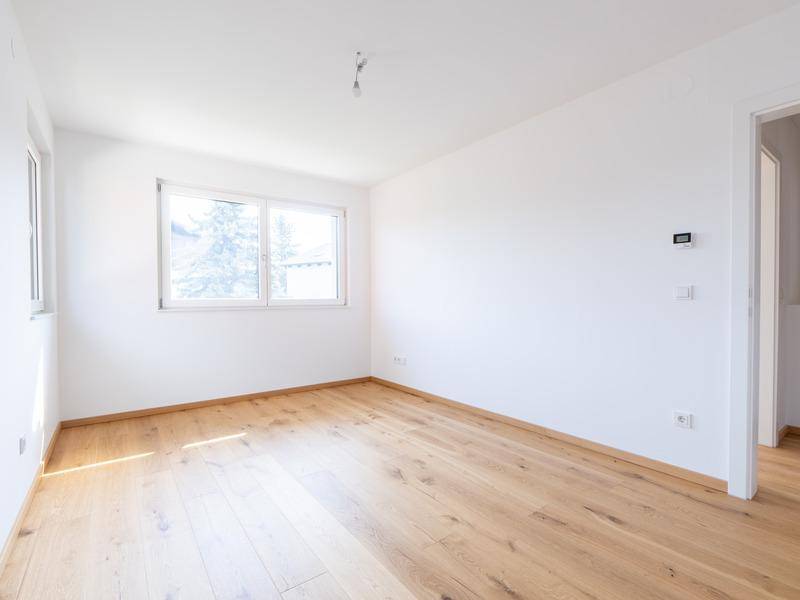 Heller, leerer Raum mit Holzboden und großem Fenster, bereit zur individuellen Gestaltung.