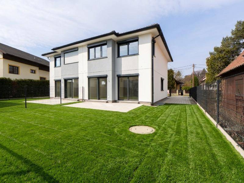 Modernes Neubau-Doppelhaus mit gepflegtem Rasen und großzügiger Terrasse im Garten.
