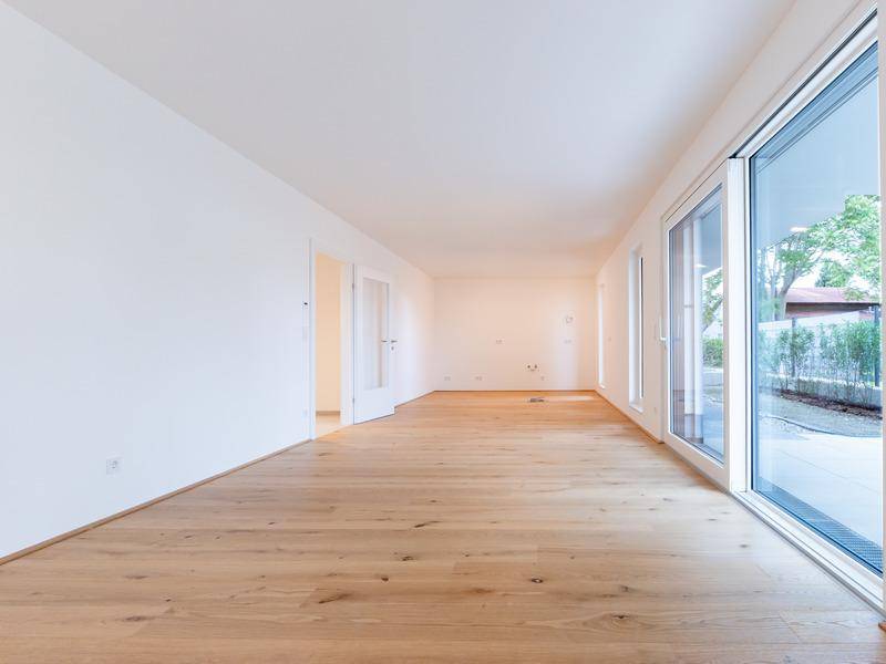 Geräumiger, unmöblierter Raum mit hellem Holzboden und bodentiefen Fenstern.