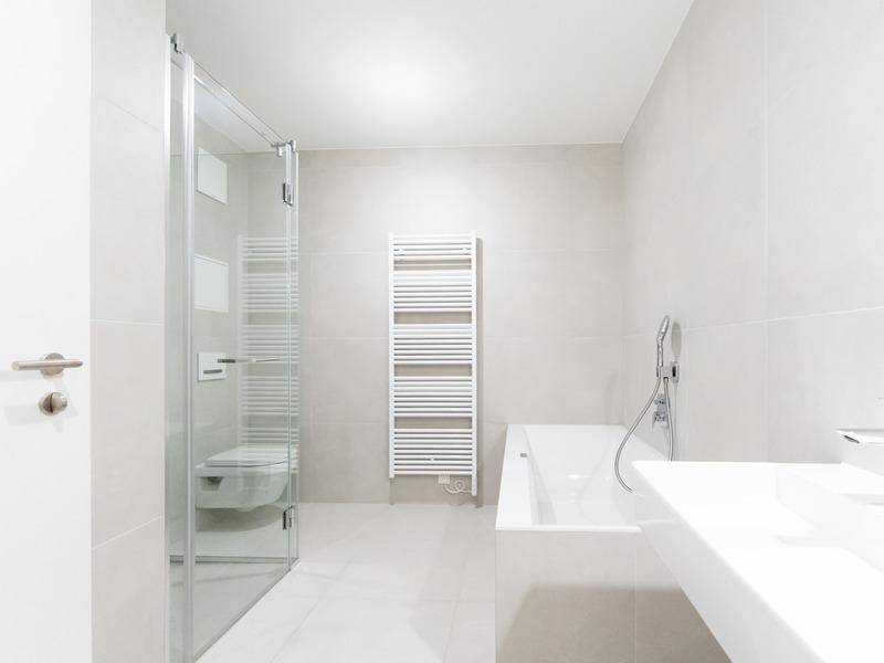 Modernes Badezimmer mit hellgrauen Fliesen, Duschkabine, Badewanne und Handtuchheizkörper.
