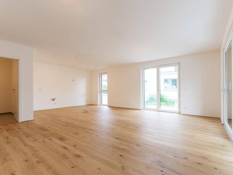 Heller Wohnraum mit Holzboden, weißen Wänden und großen Glastüren zum Außenbereich.