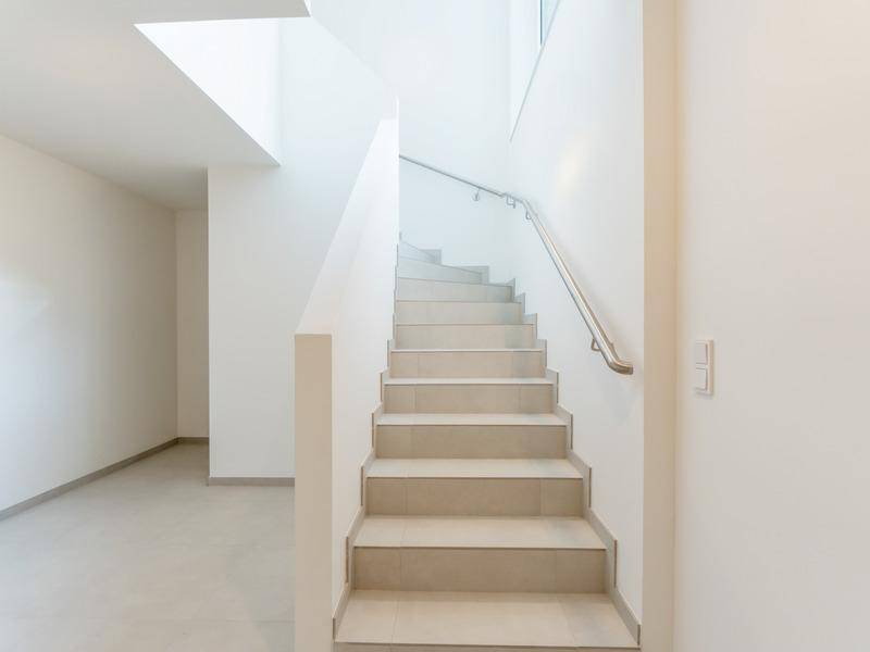 Helles, modernes Treppenhaus mit Fliesenstufen und Edelstahlgeländer, lichtdurchflutet.