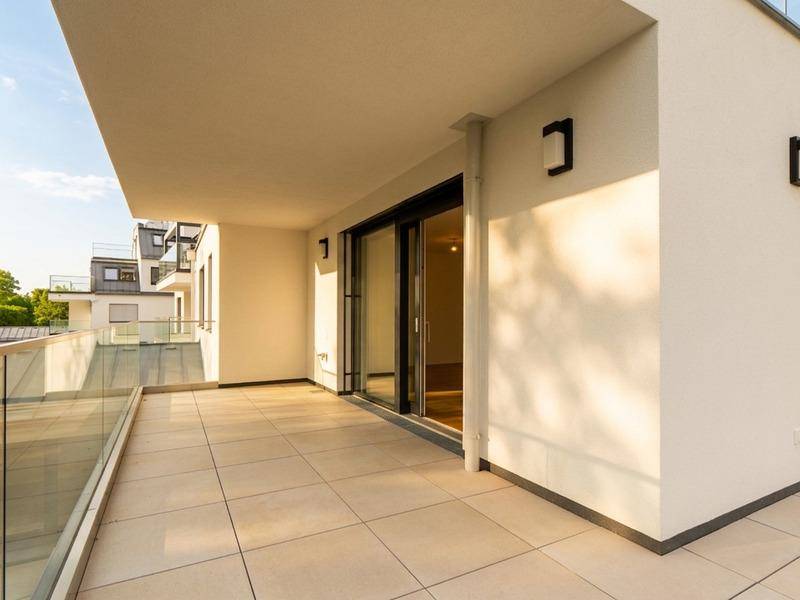 Sonniger Balkon mit modernen Fliesen, Glasgeländer und direktem Zugang zum Innenbereich durch eine Schiebetür.