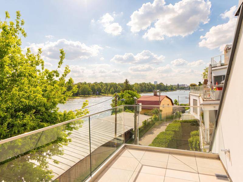 Sonnige Terrasse mit Glasgeländer und weitem Blick auf das Wasser und die grüne Umgebung.