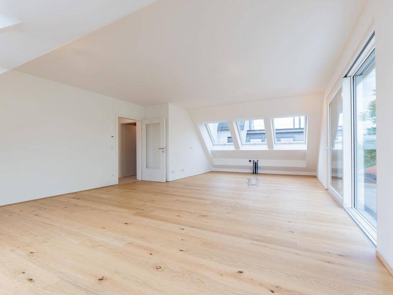 Heller Wohnraum mit Holzboden, Dachschrägen und großen Fenstern mit Zugang zur Terrasse.