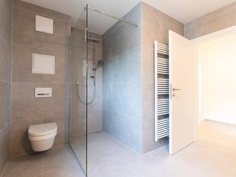 Modernes Badezimmer mit grauen Fliesen, ebenerdiger Dusche, Wand-WC und beheiztem Handtuchhalter.