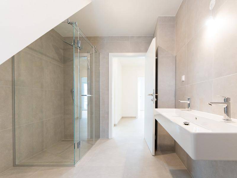 Modernes Badezimmer mit hellgrauen Fliesen, begehbarer Dusche und Doppelwaschbecken.