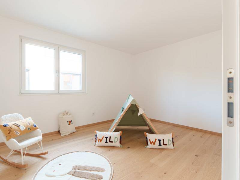 Helles Kinderzimmer mit Holzboden, Fenster und spielerischer Dekoration.