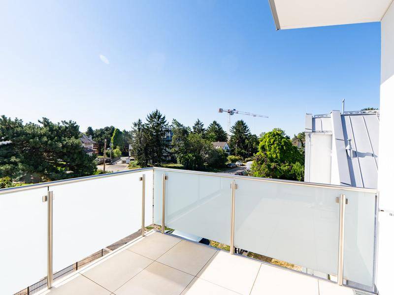 Moderner Balkon mit Glasgeländer und Fliesenboden, bietet einen Blick ins Grüne.