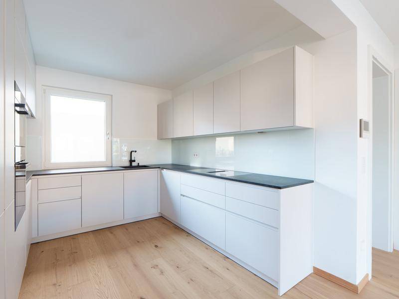Moderne weiße Einbauküche mit dunkler Arbeitsplatte und integrierten Geräten.