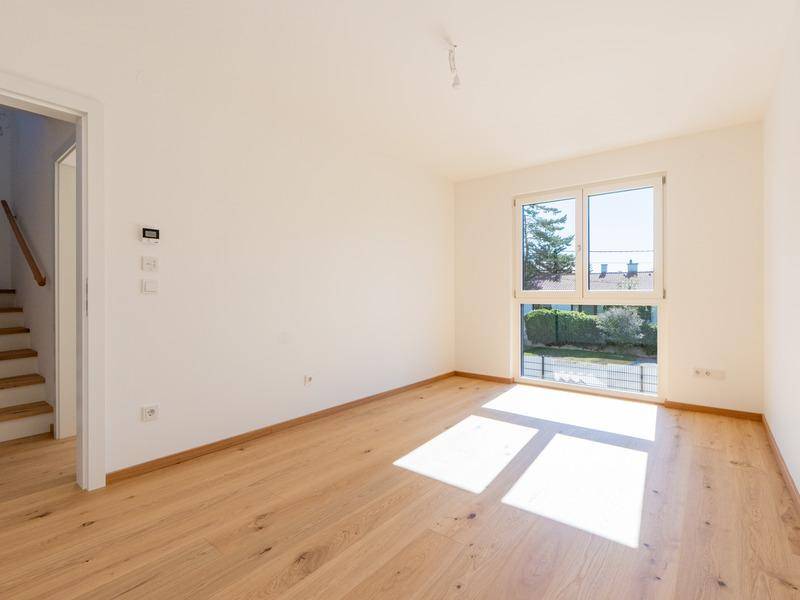 Helles Schlafzimmer mit Holzboden und großem Fenster mit Blick ins Grüne.