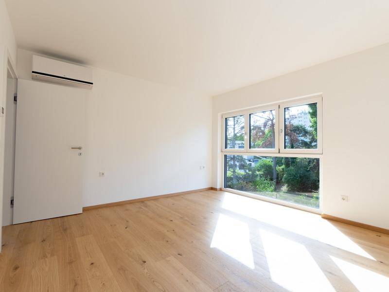 Helles Zimmer mit Holzfußboden, Klimaanlage und großem Fenster mit Grünblick.