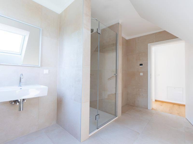 Modernes Badezimmer mit beigefarbenen Fliesen, begehbarer Dusche und Dachfenster.