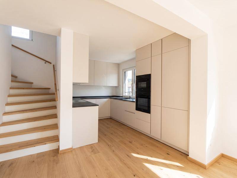 Moderne Einbauküche mit hellen Fronten, integriertem Backofen und Holztreppe.
