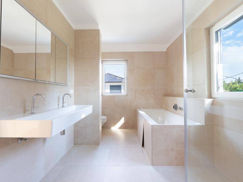 Modernes Badezimmer mit beigefarbenen Fliesen, Doppelwaschbecken und Badewanne.