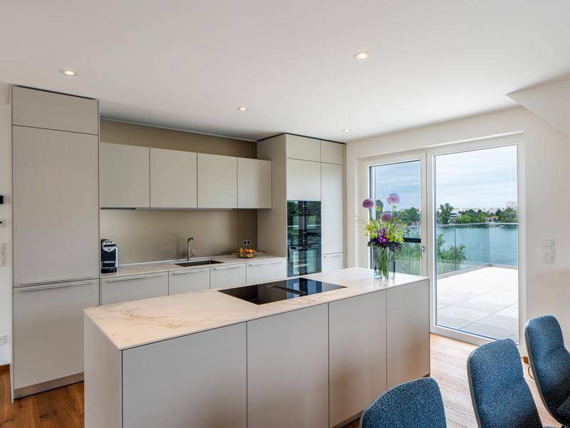 Elegante Einbauküche mit Kücheninsel, modernen Geräten und direktem Zugang zur Terrasse mit Seeblick.