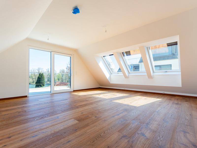 Heller Raum mit Holzboden, Dachschrägen, Dachfenstern und Zugang zu einem Außenbereich.