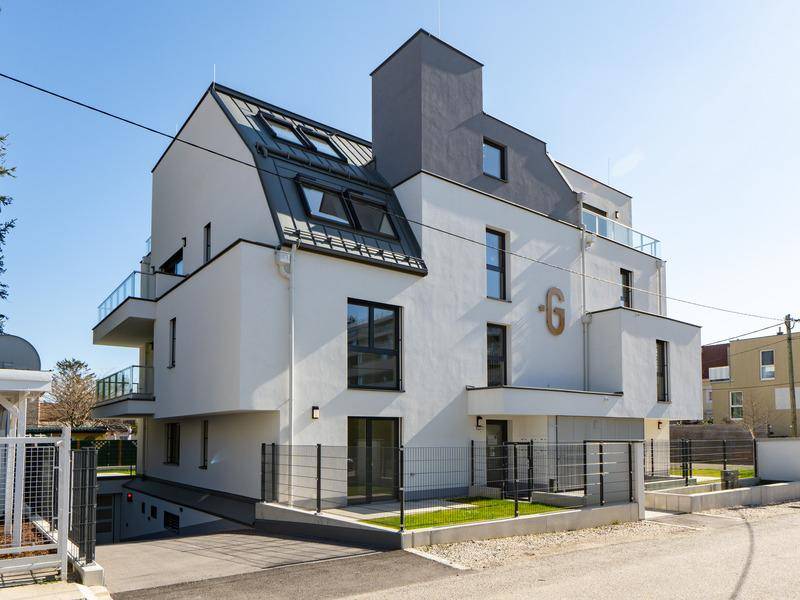 Modernes Wohngebäude mit weißer Fassade, dunklem Dach und mehreren Balkonen sowie einer Garagenzufahrt.