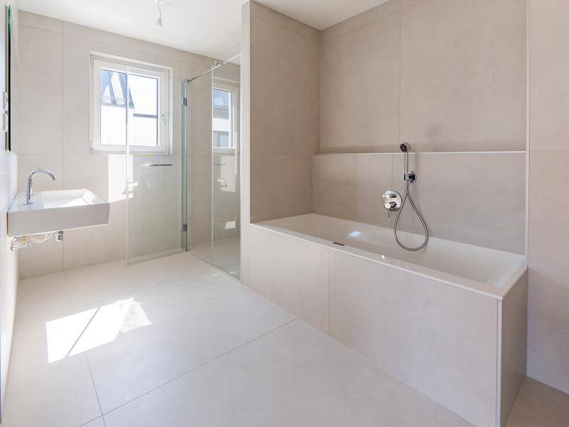 Modernes Badezimmer mit großen Fliesen, Badewanne, begehbarer Dusche und Fenster.