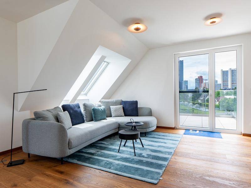 Gemütliches Wohnzimmer mit Sofa, Teppich, Dachschrägen und großen Fenstern mit Stadtblick.