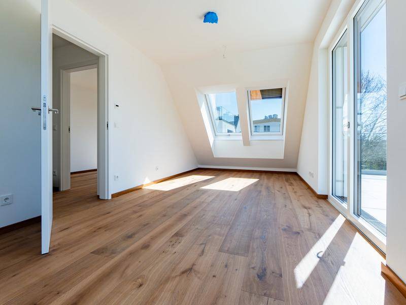 Lichtdurchfluteter Raum mit Holzboden, Dachschrägen, Dachfenstern und Zugang zur Terrasse.