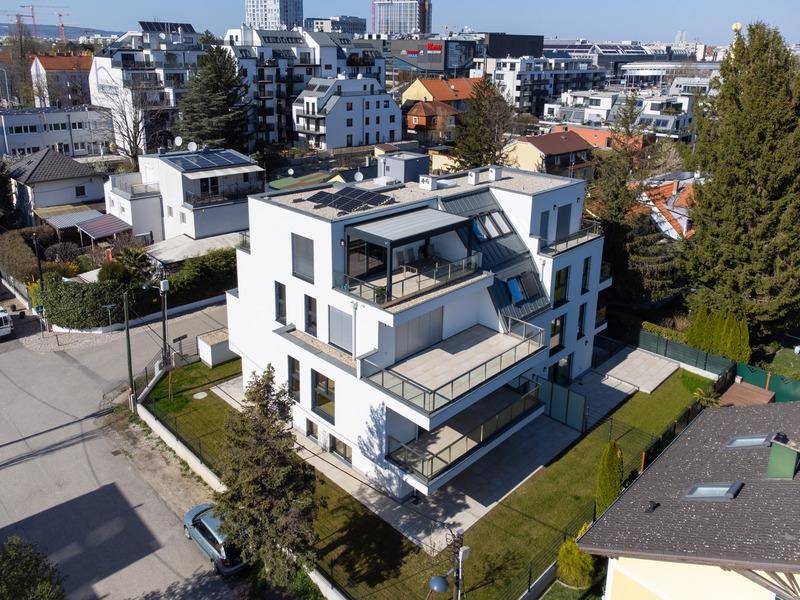 Luftaufnahme eines modernen Wohngebäudes mit Photovoltaikanlage auf dem Dach und umliegenden Grünflächen.