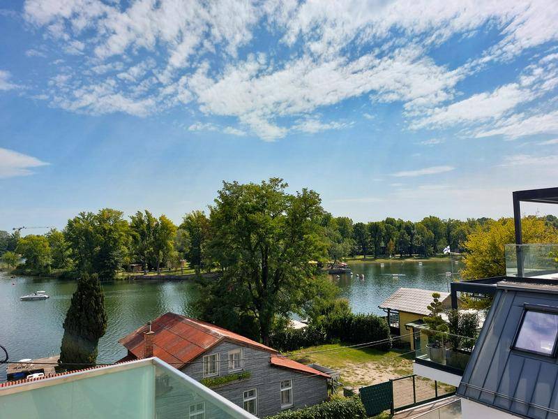 Panoramablick von einem Balkon auf einen ruhigen See mit üppiger Vegetation und Häusern.