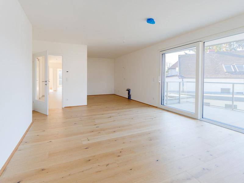Heller, leerer Wohnraum mit Eichenparkettboden und großen Schiebetüren zum Balkon.