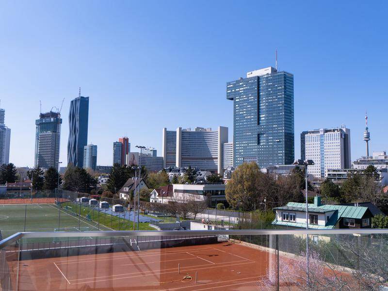 Blick von einem Balkon auf die moderne Stadtkulisse mit Hochhäusern und einem Tennisplatz im Vordergrund.