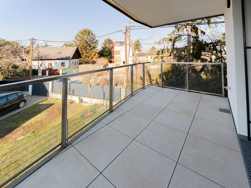 Großer Balkon mit Fliesenboden und moderner Glas-Metall-Brüstung, bietet Ausblick ins Grüne.
