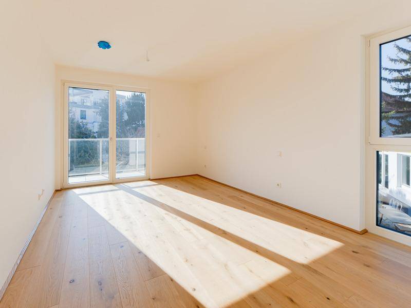 Sonniger Wohnraum mit hellem Parkettboden und großen Fenstern, die viel Licht hereinlassen.