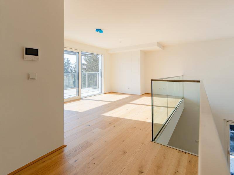 Lichtdurchfluteter Raum mit Holzboden, großem Schiebefenster und Zugang zu einem Balkon.