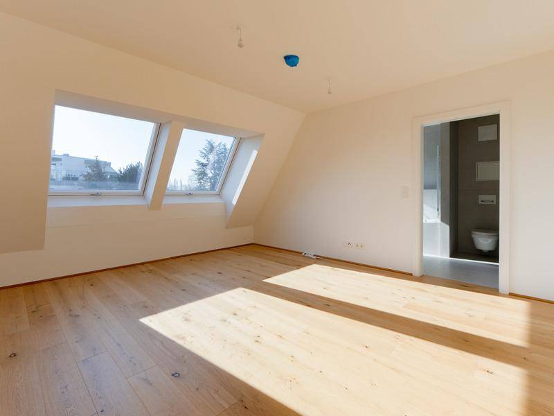 Helles Schlafzimmer mit Holzboden, Dachfenstern und direktem Zugang zum Badezimmer.