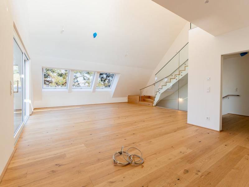 Heller, unmöblierter Raum mit Holzboden, großen Dachfenstern und moderner Glastreppe.