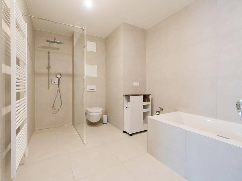 Modernes Badezimmer mit begehbarer Dusche, Badewanne, Wand-WC und hellen Fliesen.