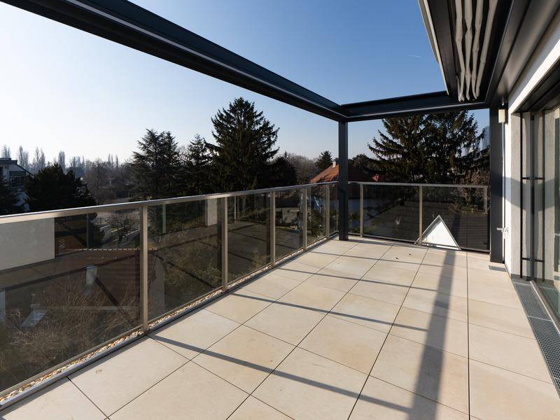 Geräumiger Balkon mit Fliesenboden, Glasgeländer und weitem Blick ins Grüne.
