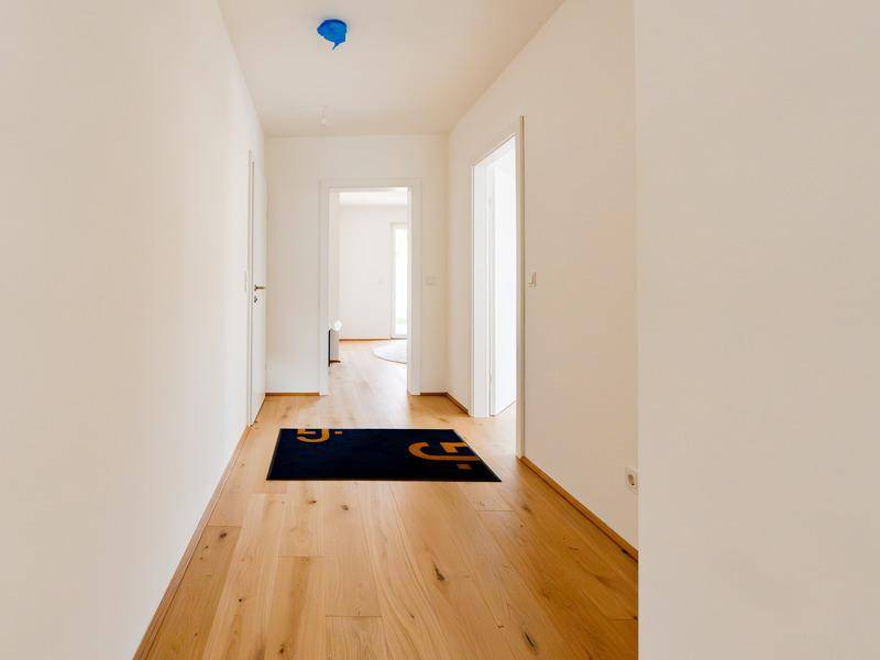 Heller Flur mit Holzboden und weißen Wänden, der zu weiteren Räumen führt.