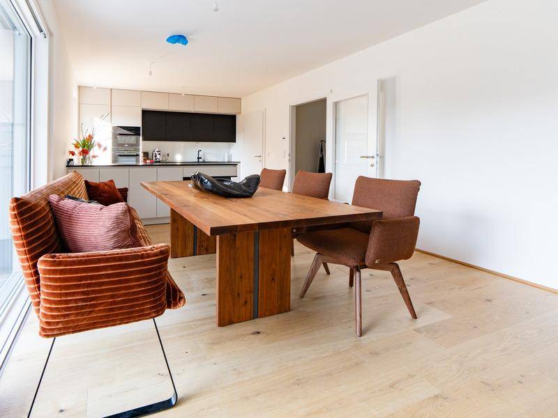 Heller Essbereich mit Holztisch und modernen Stühlen, offen zur Küche, mit Holzboden.