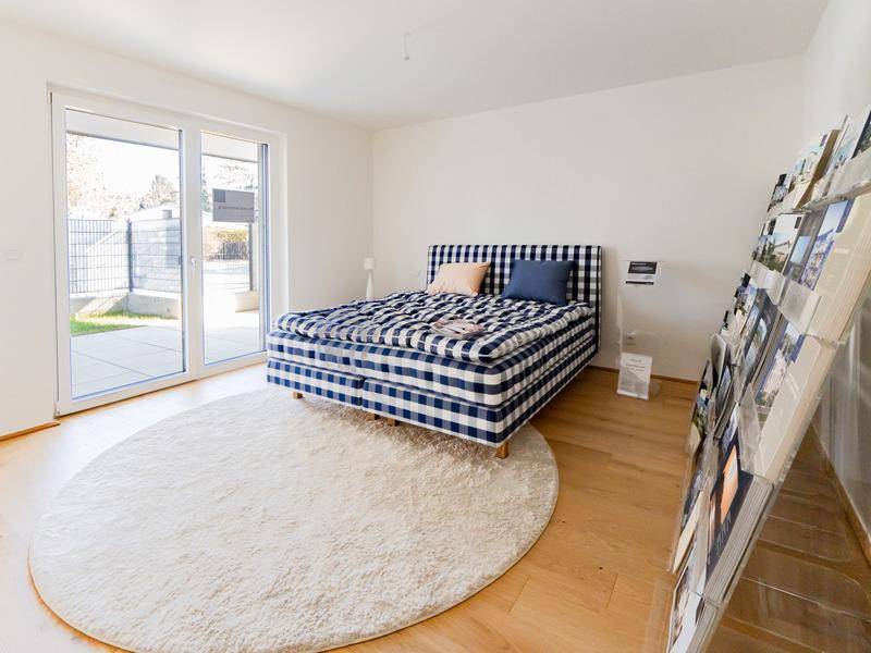 Helles Schlafzimmer mit modernem Bett, Holzboden und großen Schiebetüren zum Außenbereich.