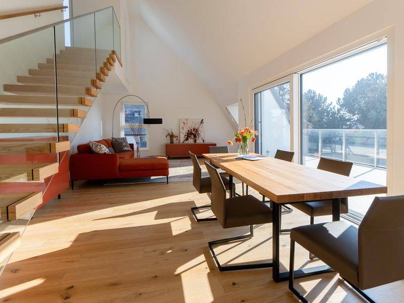 Heller offener Wohn-Essbereich mit Holzboden, moderner Treppe und Zugang zur Terrasse.