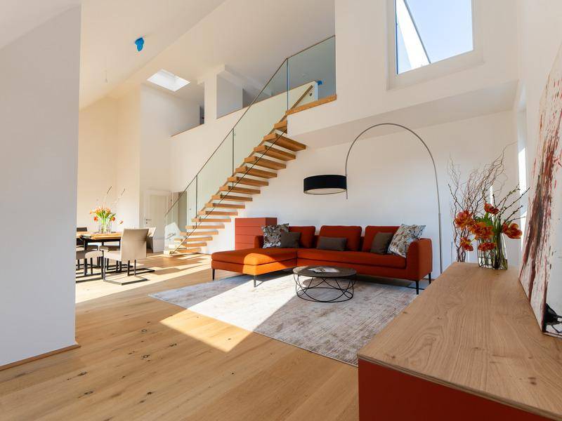 Lichtdurchflutetes Wohnzimmer mit rotem Sofa, modernem Design und eleganter Treppe.