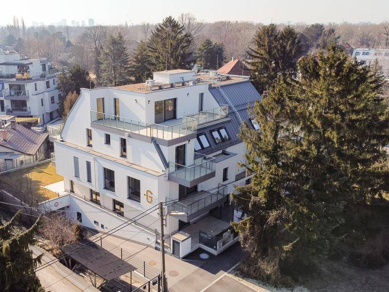 Moderne Wohnanlage mit mehreren Balkonen und Terrassen, umgeben von Bäumen in städtischer Umgebung.